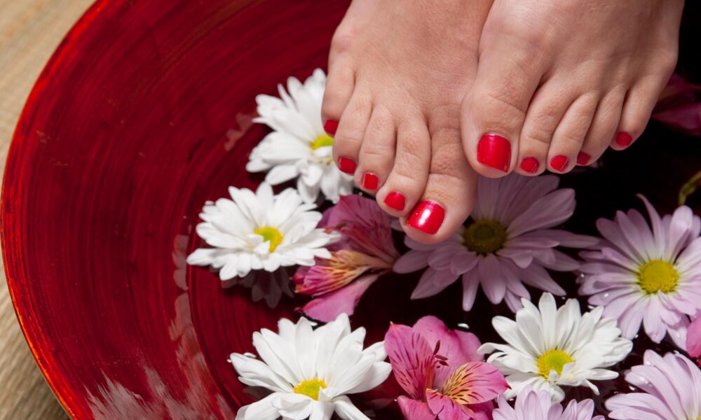 Füße mit roten Zehennägeln und Blumen im Hintergrund