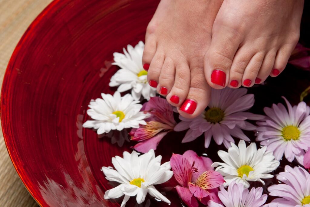 Füße mit roten Zehennägeln und Blumen im Hintergrund