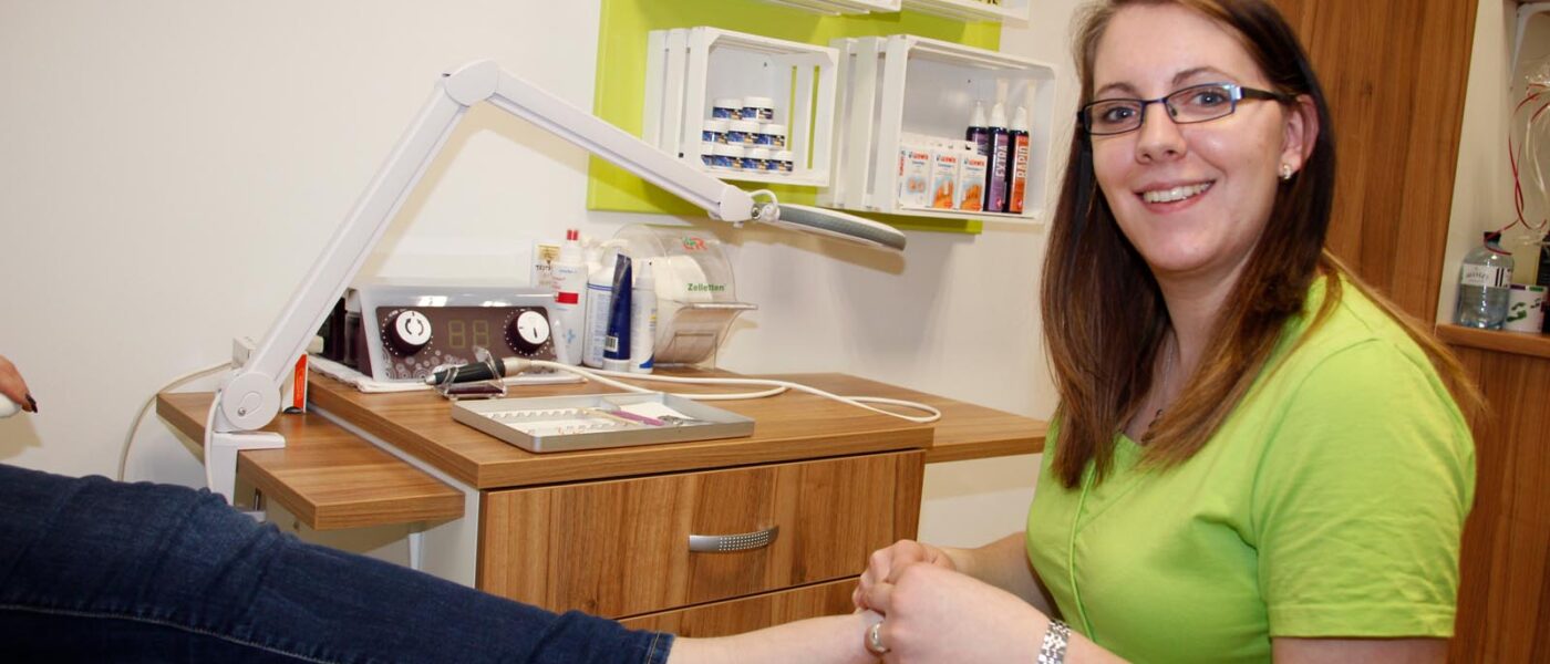 Regina am Behandlungssessel mit Fuß in der Hand